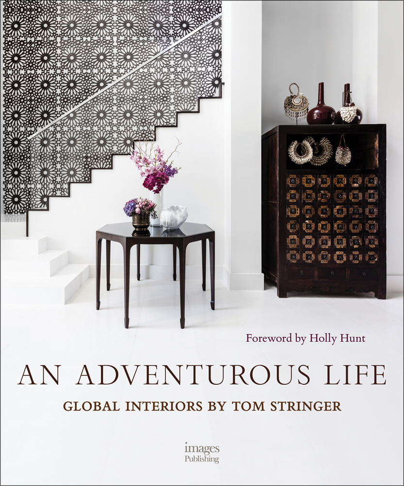 Book cover of An Adventurous Life: Global Interiors by Tom Stringer, with a white interior hallway with dark wood table with vases of flowers. Published by Images Publishing.