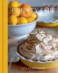 Meringue pie in dish with bowl of oranges in background with County Fair Nostalgic Blue Ribbon Recipes from America’s Small Towns in white font above