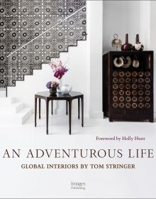 Book cover of An Adventurous Life: Global Interiors by Tom Stringer, with a white interior hallway with dark wood table with vases of flowers. Published by Images Publishing.