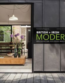 Large open door to interior, low table with purple alliums in vase, hanging light fittings, British + Irish Modern in white and green font