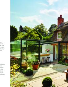 Large open door to interior, low table with purple alliums in vase, hanging light fittings, British + Irish Modern in white and green font