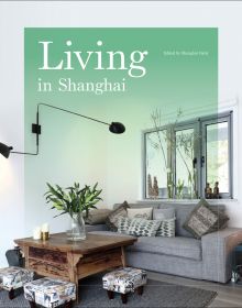 Interior room, grey sofa, wood table with vase of lilies, 3 footstools, Living in Shanghai in white font on mint green cover