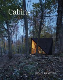 Modern cabin, with interior lights on, in forest at dusk, Cabins in white font to upper left.