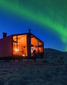 Book cover of Cabins: Escape to Nature, with modern cabin in a forest, with interior lights on. Published by Images Publishing.