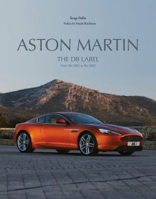Orange Aston Martin Virage Coupé, mountain scape behind, ASTON MARTIN THE DB LABEL, in grey font above.